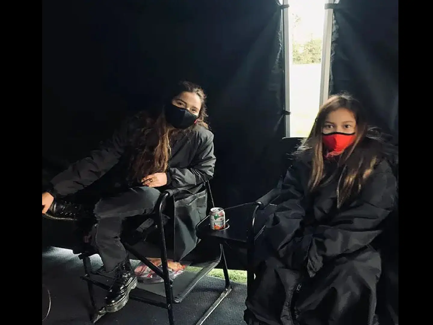 Two women sitting in a chair wearing masks.