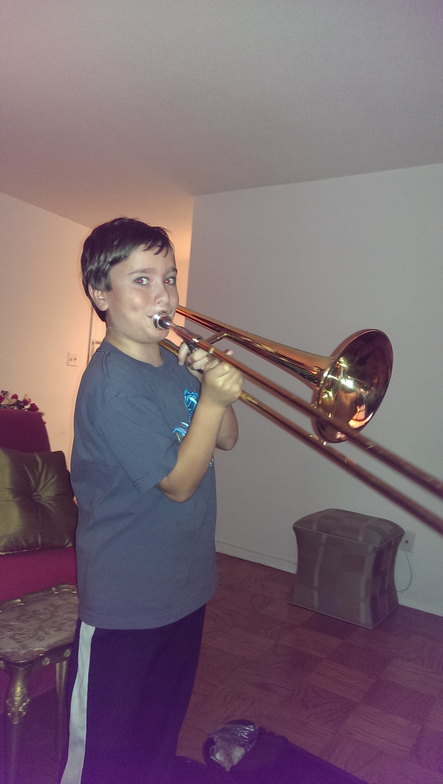 A boy playing the trombone in his living room.